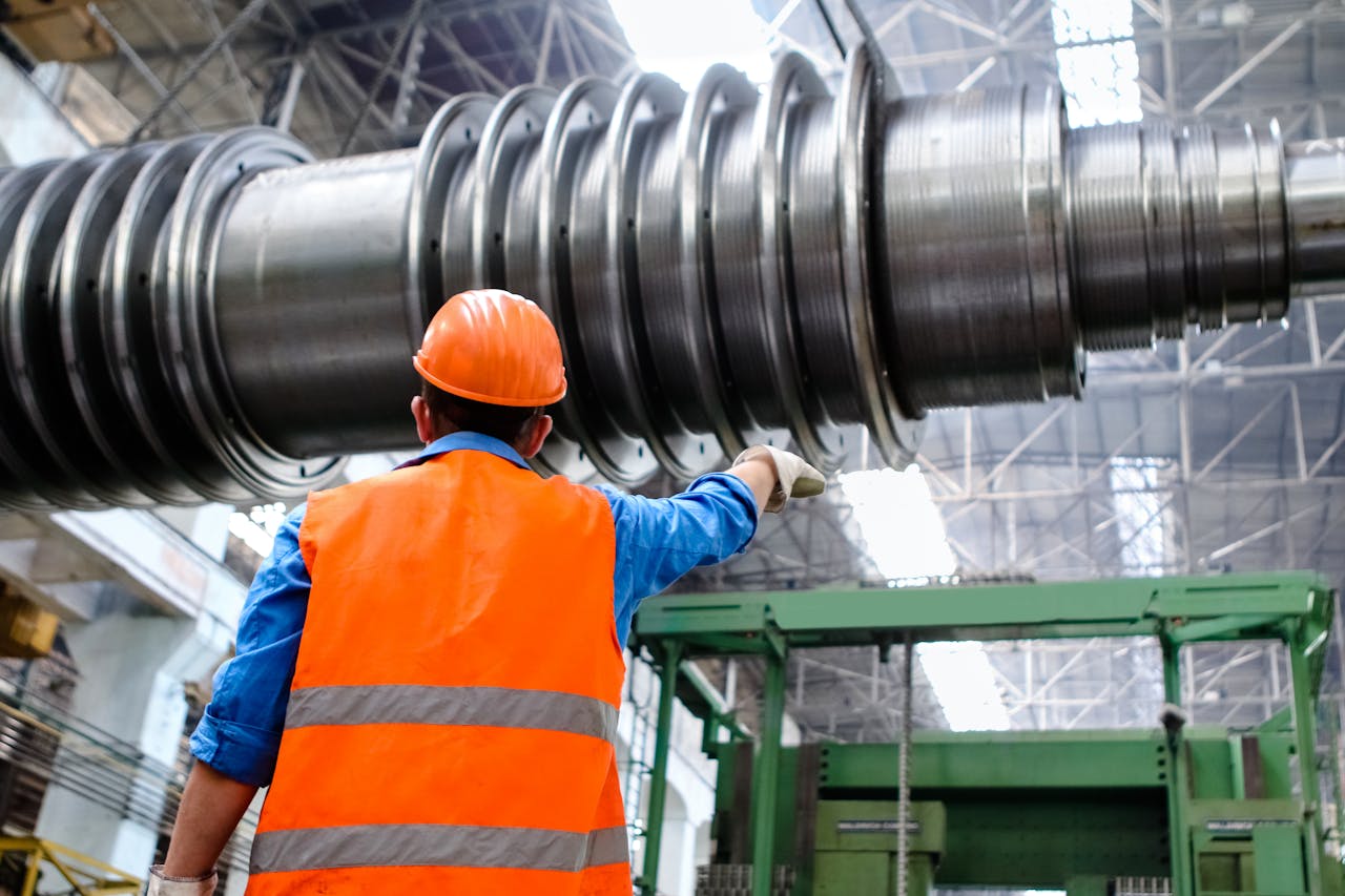 Home Engineer in high visibility vest and hard hat inspecting large machinery in factory setting.